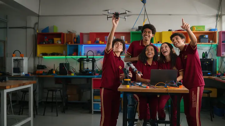 Alunos de uniforme pilotam um drone e montam um braço robótico na sala maker